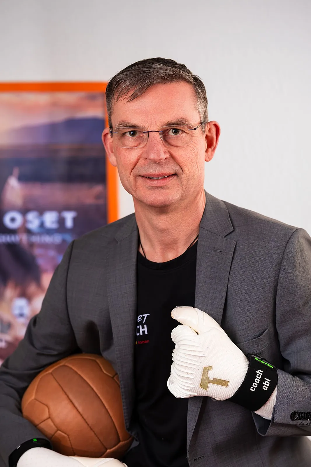 Markus Ebi im Sakko, eine Torwarthandschuh-Faust vor der Brust, den Lederball im Arm.